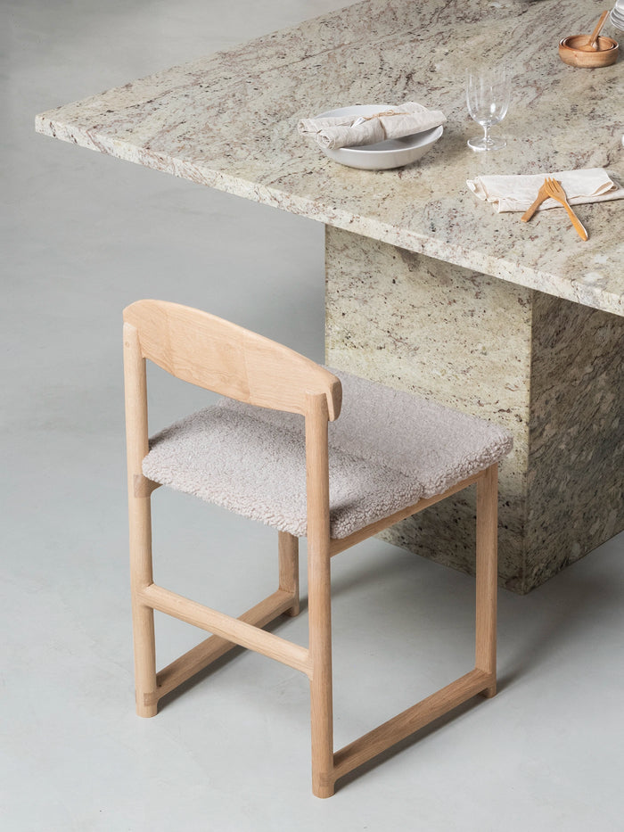 Dining chair Karin with oak wood frame and greige bouclé cushion beside a stone dining table.