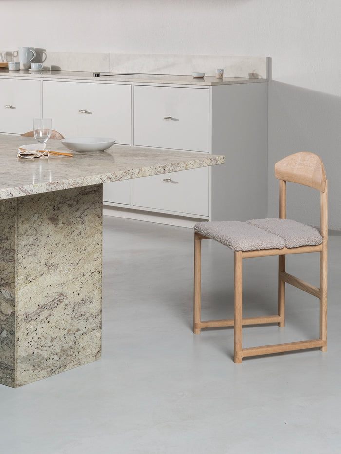 Dining chair Karin with oak wood frame and greige bouclé cushion in modern kitchen setting.