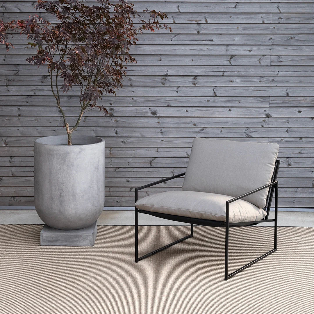 Kenny Lounge Chair in black with fossil acrylic, set against a wooden wall and a modern planter.