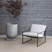 Kenny lounge chair in black with white cushions, paired with a modern marble planter on a textured floor.