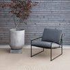 Kenny lounge chair in black with onyx acrylic material, placed beside a modern concrete planter and wooden wall.