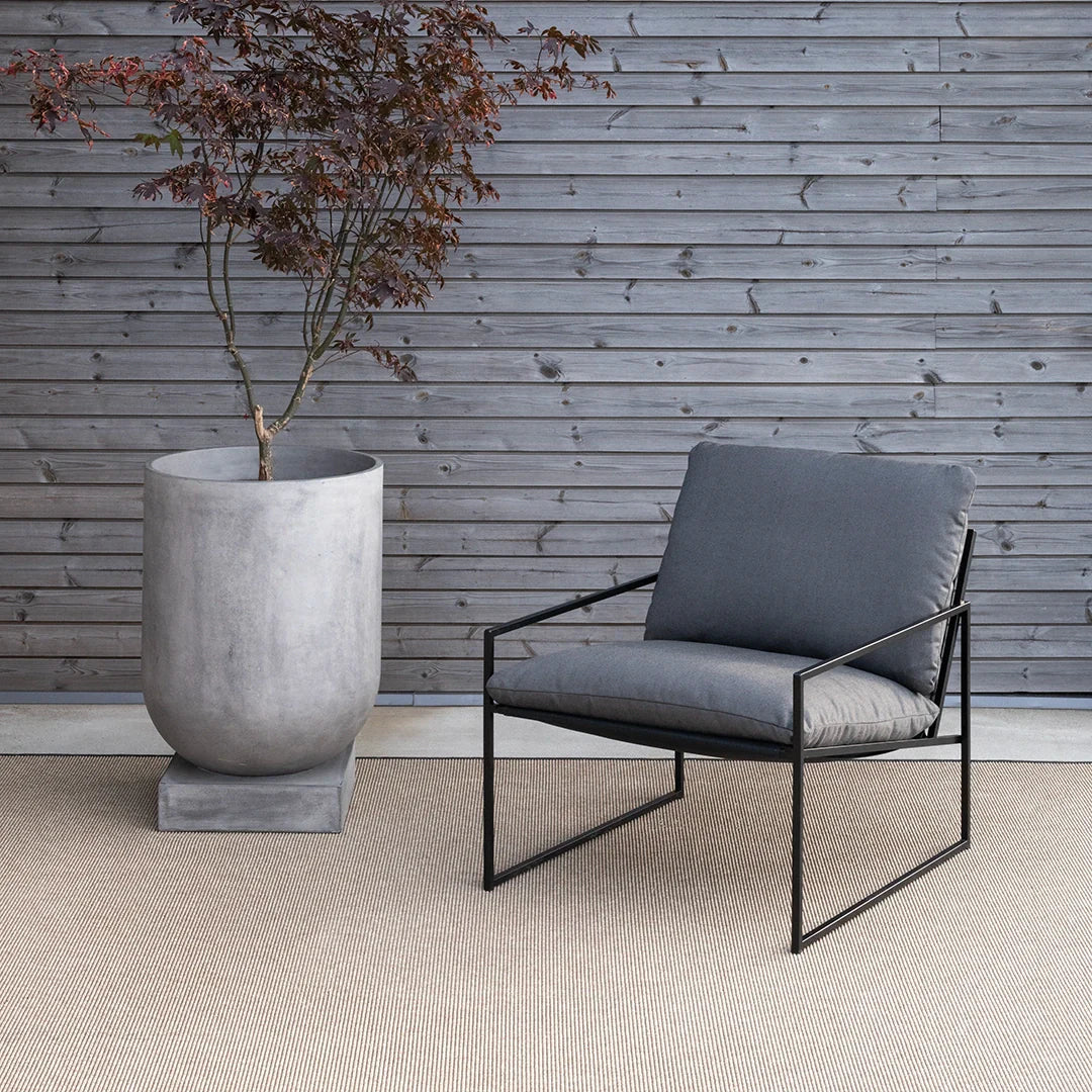 Kenny lounge chair in black with onyx acrylic material, placed beside a modern concrete planter and wooden wall.