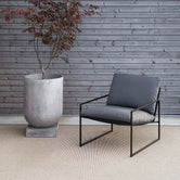 Outdoor lounge chair Kenny with black frame and onyx cushion next to modern planter.