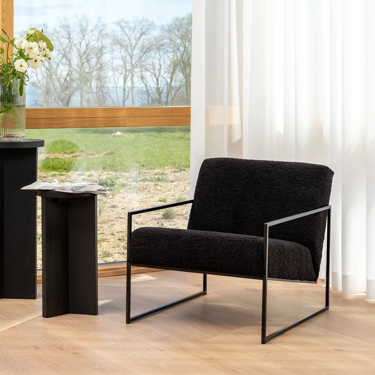 Kent armchair in black bouclé beside a sleek table, showcasing minimalist Scandinavian design in a bright interior.