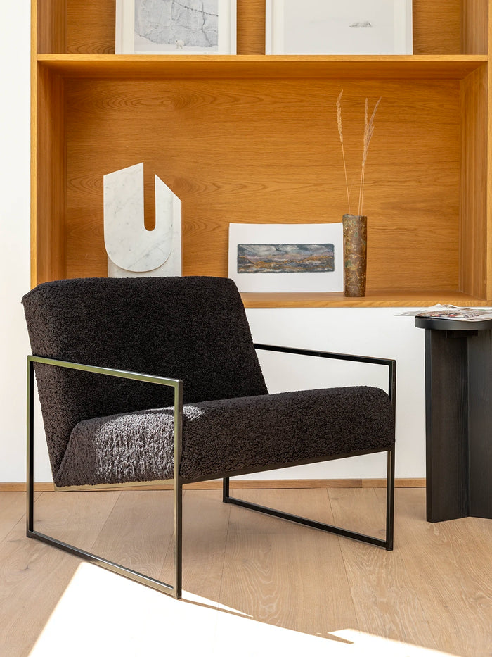 Armchair Kent in black frame with black bouclé cushion in minimalist Scandinavian design setting.