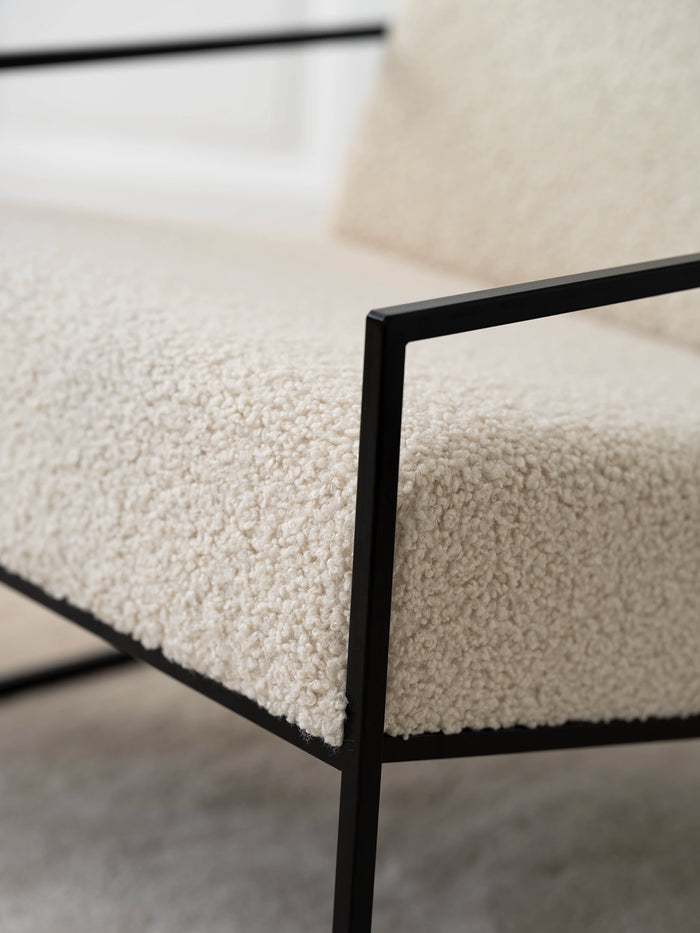 Close-up of the Armchair Kent featuring a soft ivory bouclé cushion and sleek black frame.