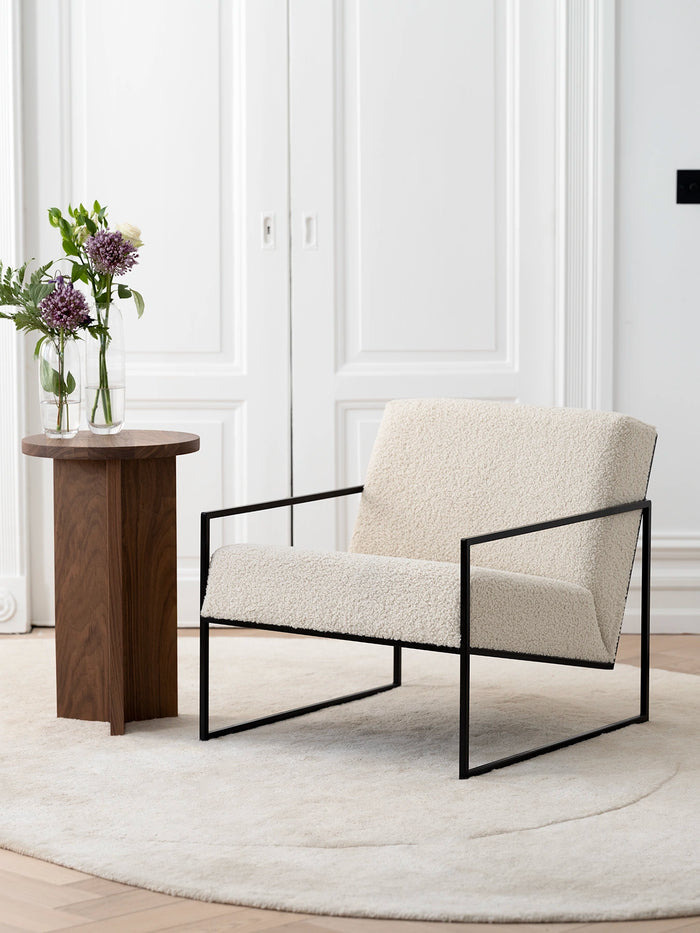 Armchair Kent – Black Frame – Ivory Bouclé Cushion in a minimalist interior setting with a side table and flowers.