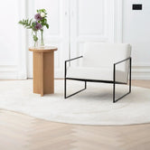 Armchair Kent in ivory leather with black frame beside a wooden side table in a stylish, modern interior.
