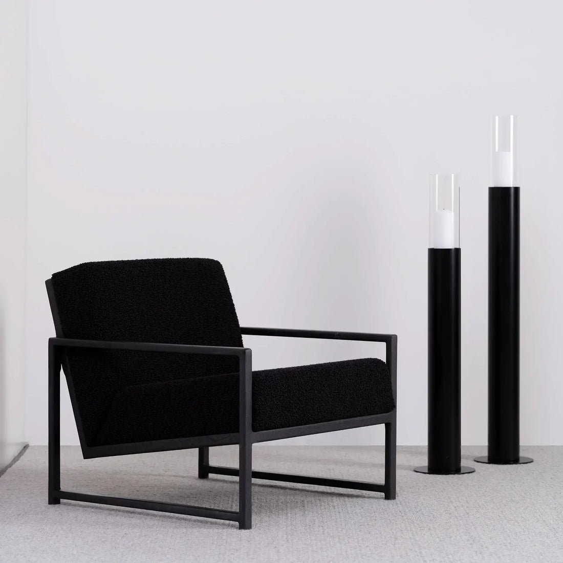 Armchair Einar in black oak frame and black bouclé cushion, minimalist design, paired with modern candle holders.