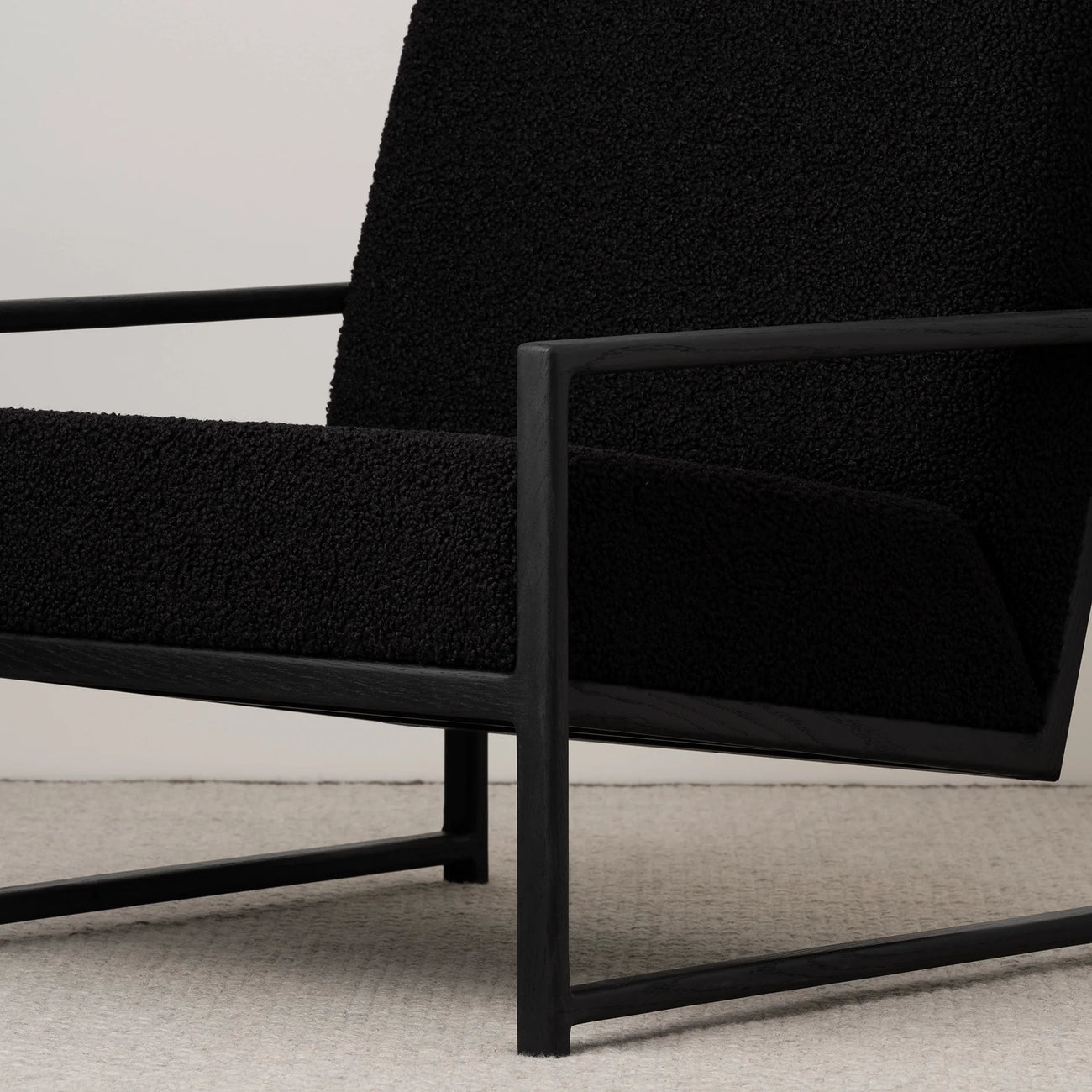 Minimalist black oak armchair with a black bouclé seat, showcasing modern design and relaxed support.