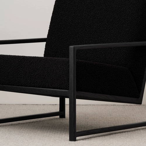 Minimalist black oak armchair with a black bouclé seat, showcasing modern design and relaxed support.