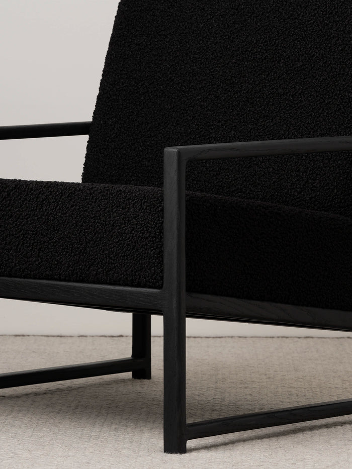Armchair Einar in black oak frame with black bouclé cushion, showcasing minimalist design and relaxed support.