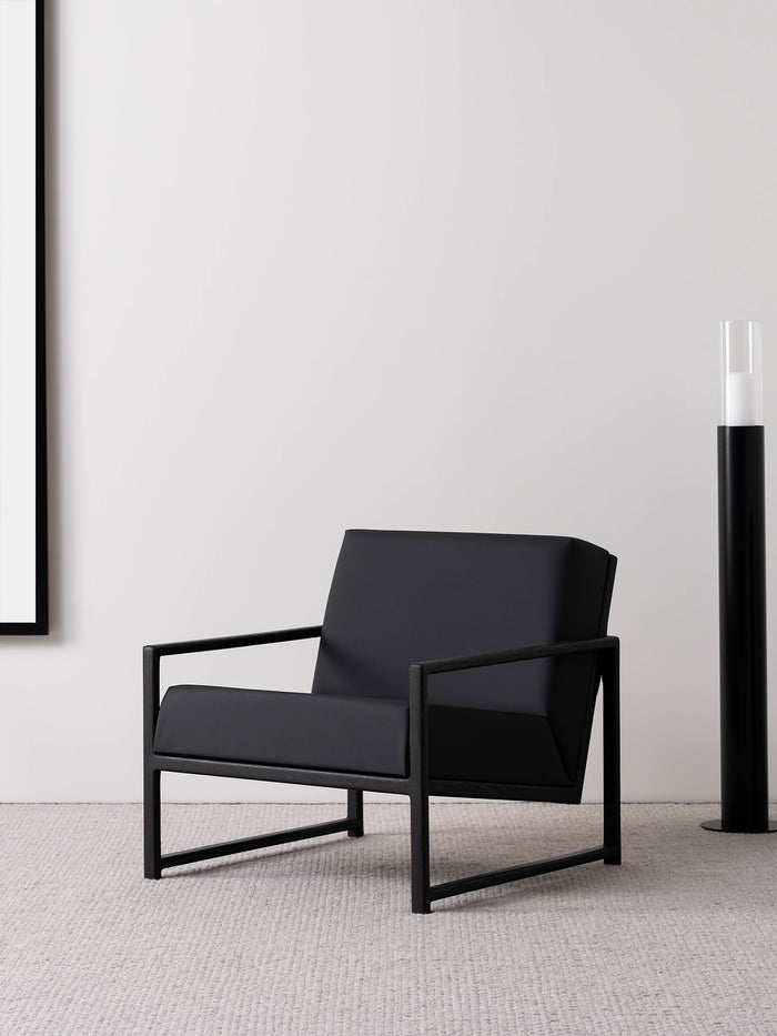 Armchair Einar with black oak frame and jade black leather cushion in modern living space.