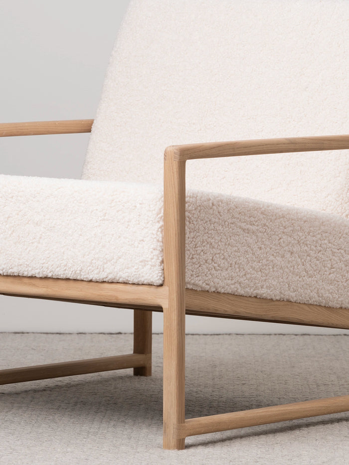 Armchair Einar with oak frame and ivory bouclé cushion for modern living spaces.