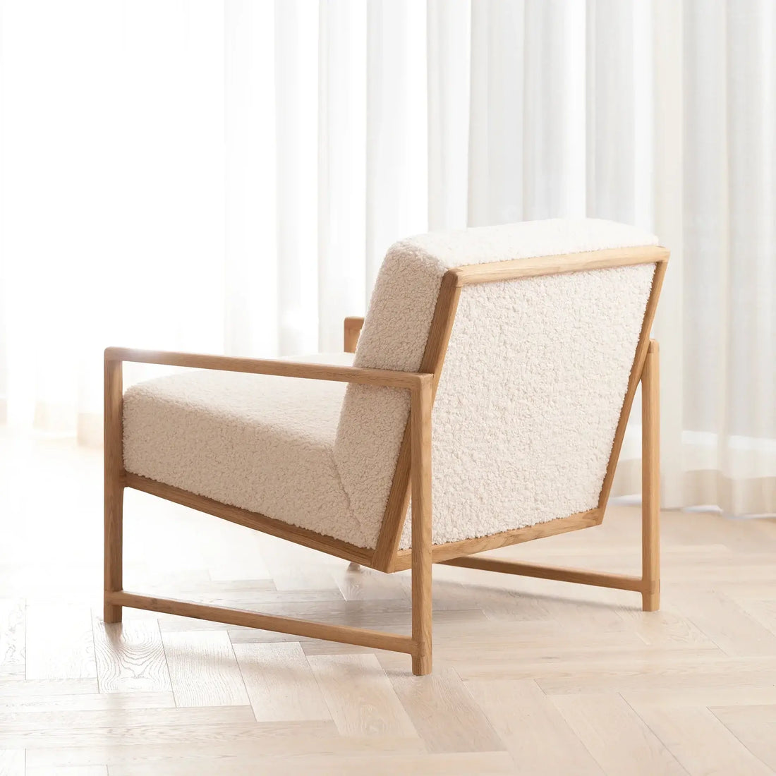 Armchair Einar with oak frame and ivory bouclé cushion in a bright modern living room.