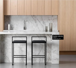 Two black bar stools in front of a marble backsplash with wooden cabinets and an illustration showing needed legroom 23-26cm (9in to 10.2in) for a bar stool.