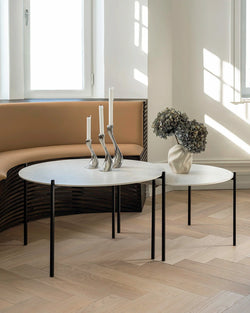 Leo round coffee table with black steel frame and Dekton stone top, styled in a Scandinavian interior with herringbone wood flooring and built-in bench seating.