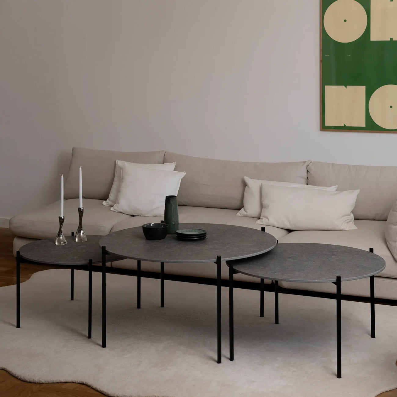 Leo Coffee Table 3-set by by Crea in Grafite Dekton with black steel frame, styled in a Scandinavian living room with modern green artwork, cream sectional, and silver candleholders. Handmade designer coffee tables for contemporary homes.