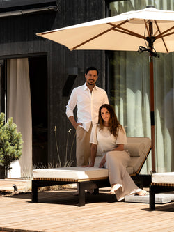 Linda and Axel at their architect-designed villa in Höllviken, seated on a Bazo sun lounger in teak and black steel beneath a cream parasol.