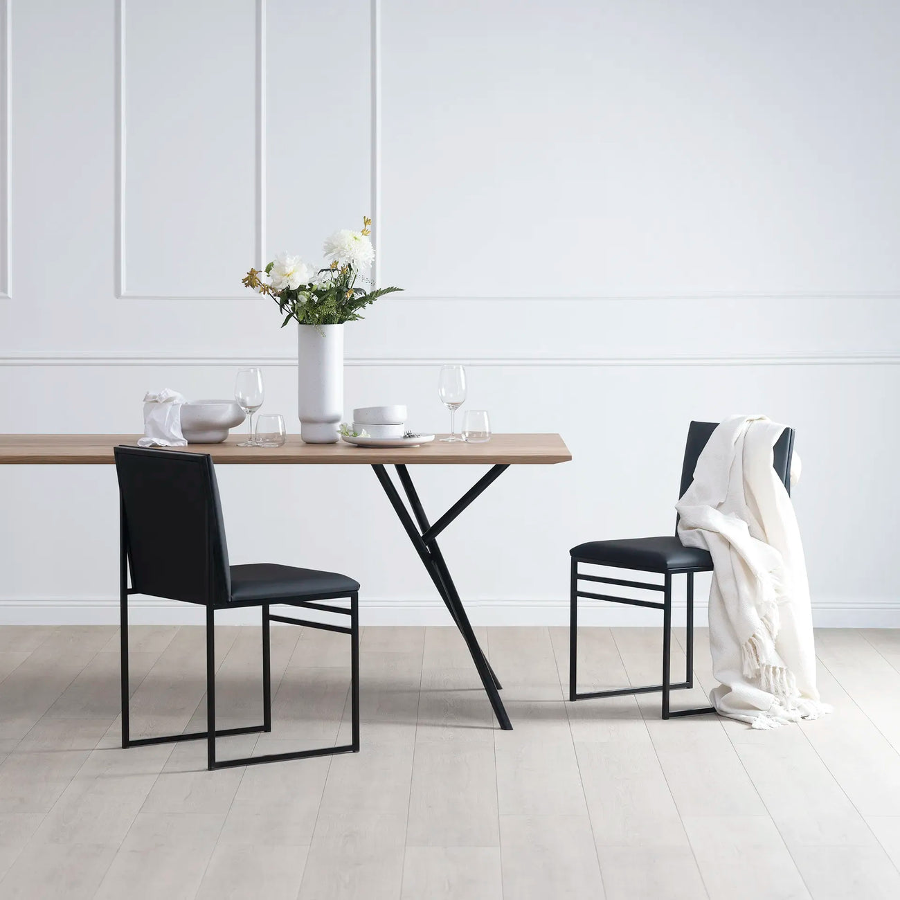 Melker dining table in black with oak top, surrounded by modern chairs and decorative vase, showcasing stylish dining setup.