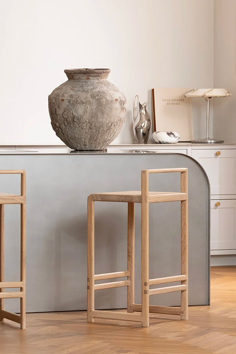 Minimalist Scandinavian kitchen with curved gray island and Ebba oak bar stools, styled with a textured ceramic vase and neutral decor.