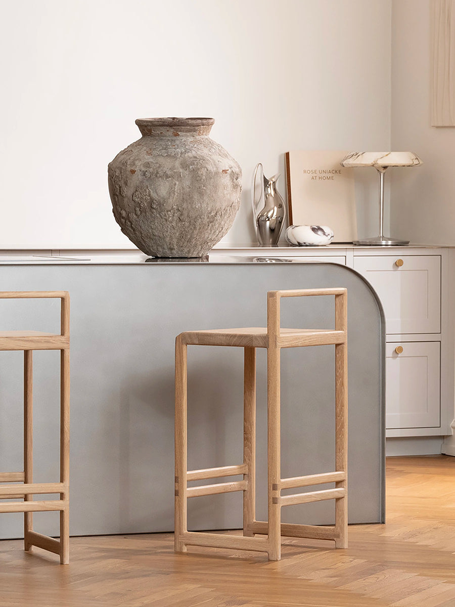Minimalist Scandinavian kitchen with curved gray island and Ebba oak bar stools, styled with a textured ceramic vase and neutral decor.