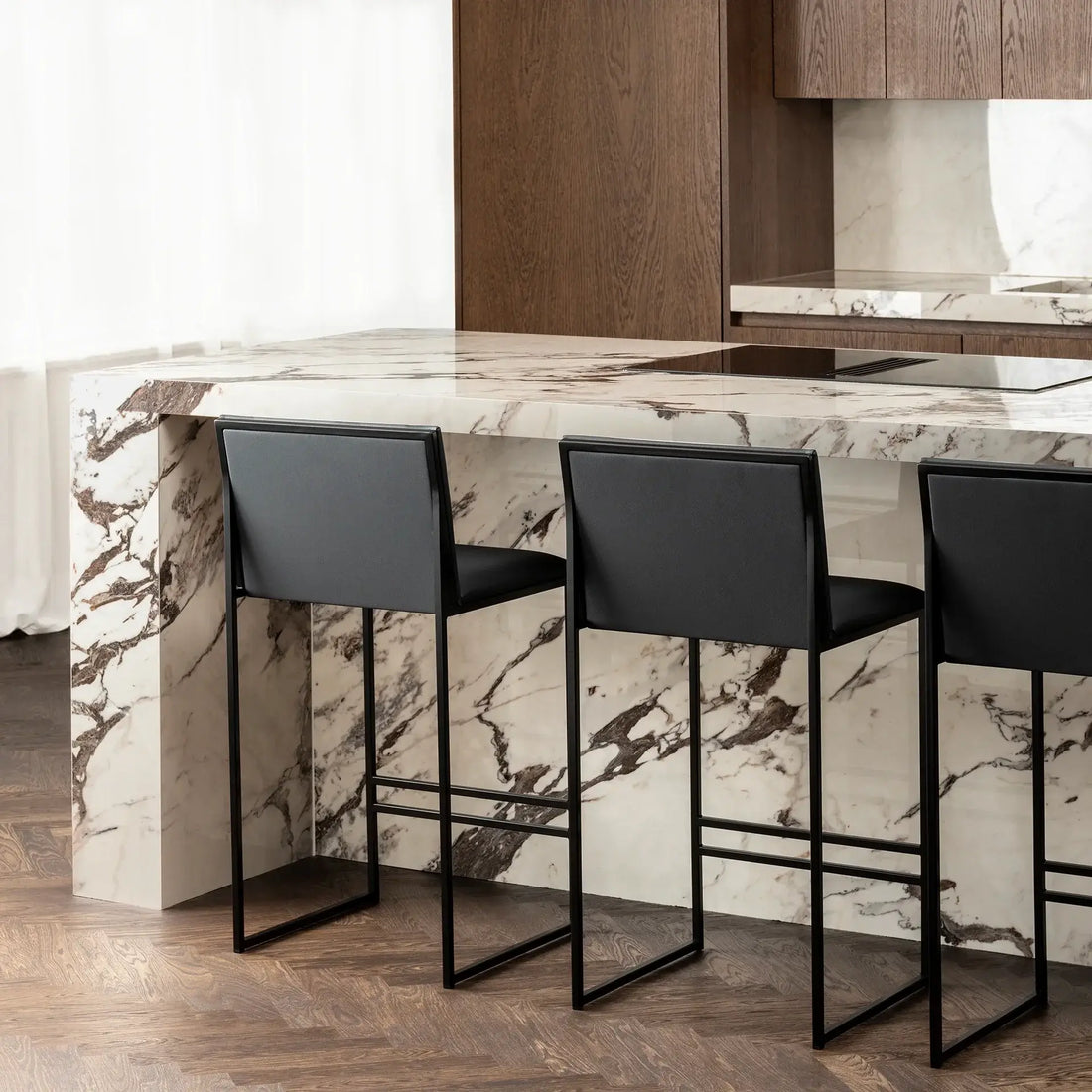 Bar Stool Philip with black frame and jade black leather cushion at a marble kitchen island.