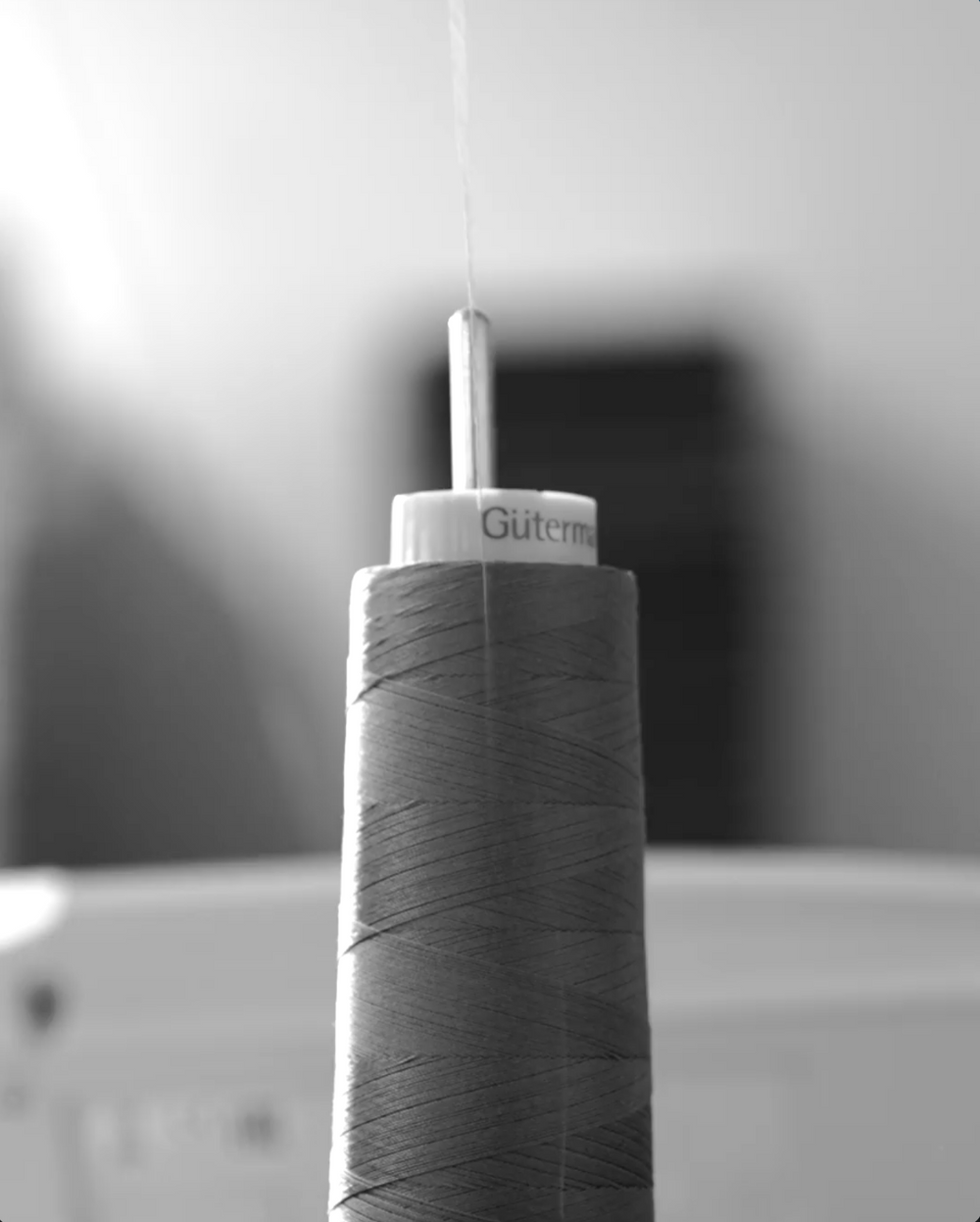 Black and white close-up of a Gütermann thread spool hanging in a the by Crea production environment, highlighting craftsmanship and textile manufacturing details.
