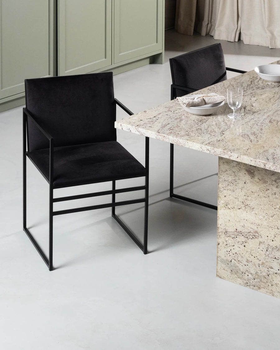 Sella Dining Chair by by Crea in jade black velvet upholstery with minimalist black steel frame, placed by a natural stone kitchen island in a Scandinavian-inspired interior.