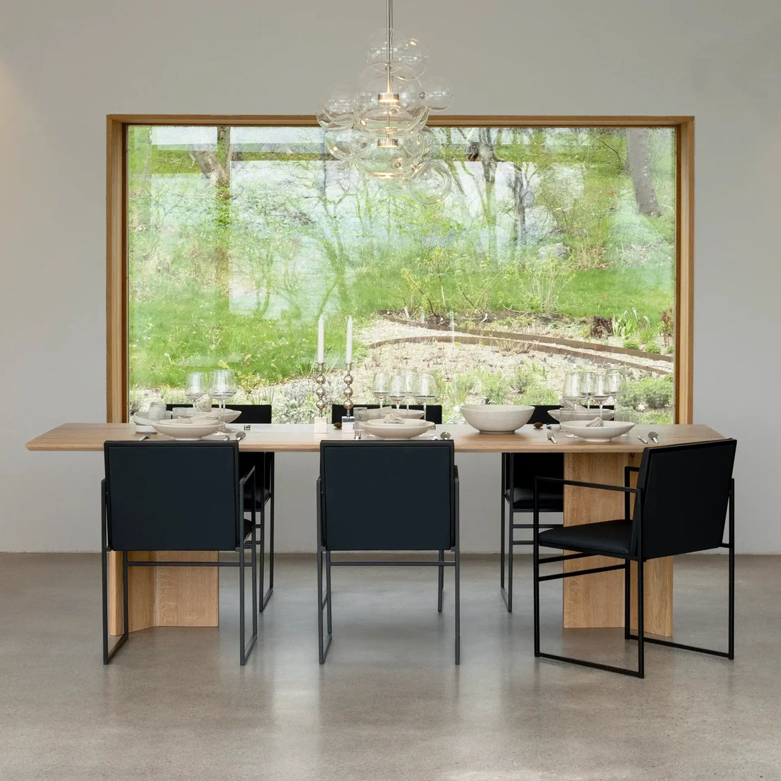Dining chair Sella in black leather around a modern dining table with large windows overlooking greenery.