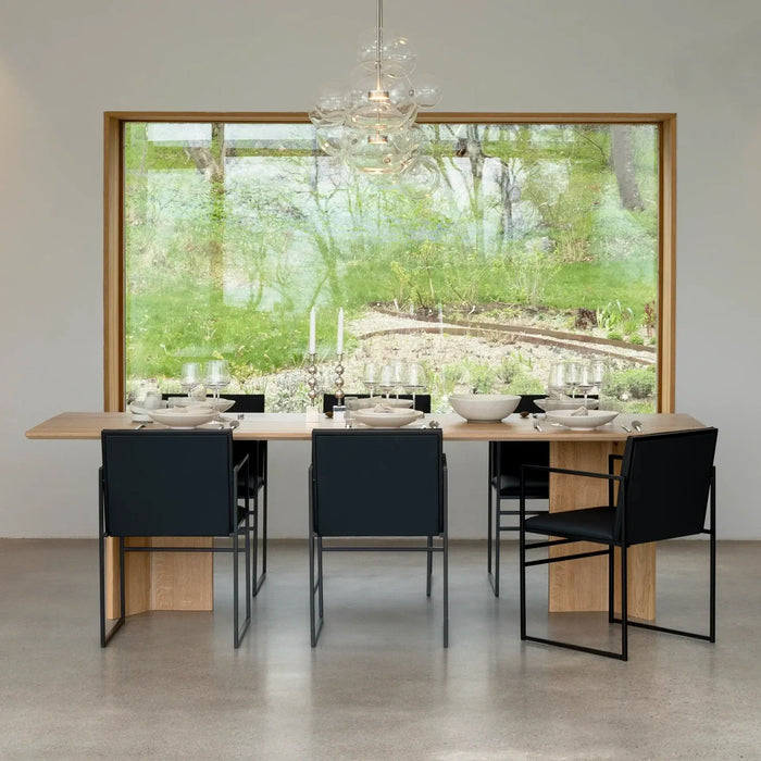 Dining chair Sella in black leather around a modern dining table with large windows overlooking greenery.