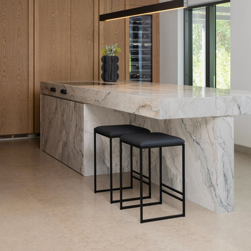 Svea bar stools in black leather at a modern kitchen island with marble countertops.