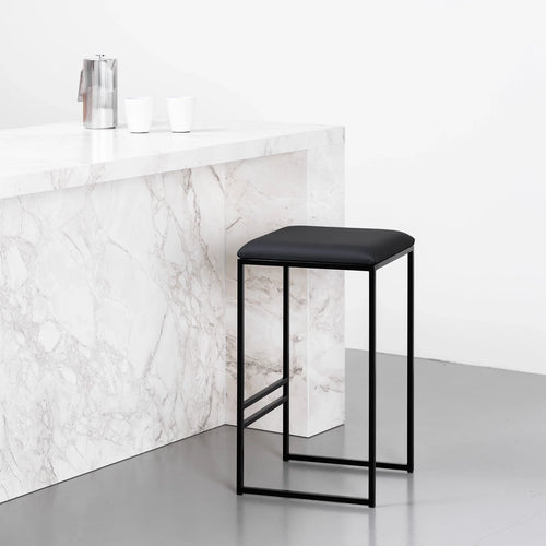 Svea bar stool in black leather with a sleek metal frame, set against a modern marble countertop.