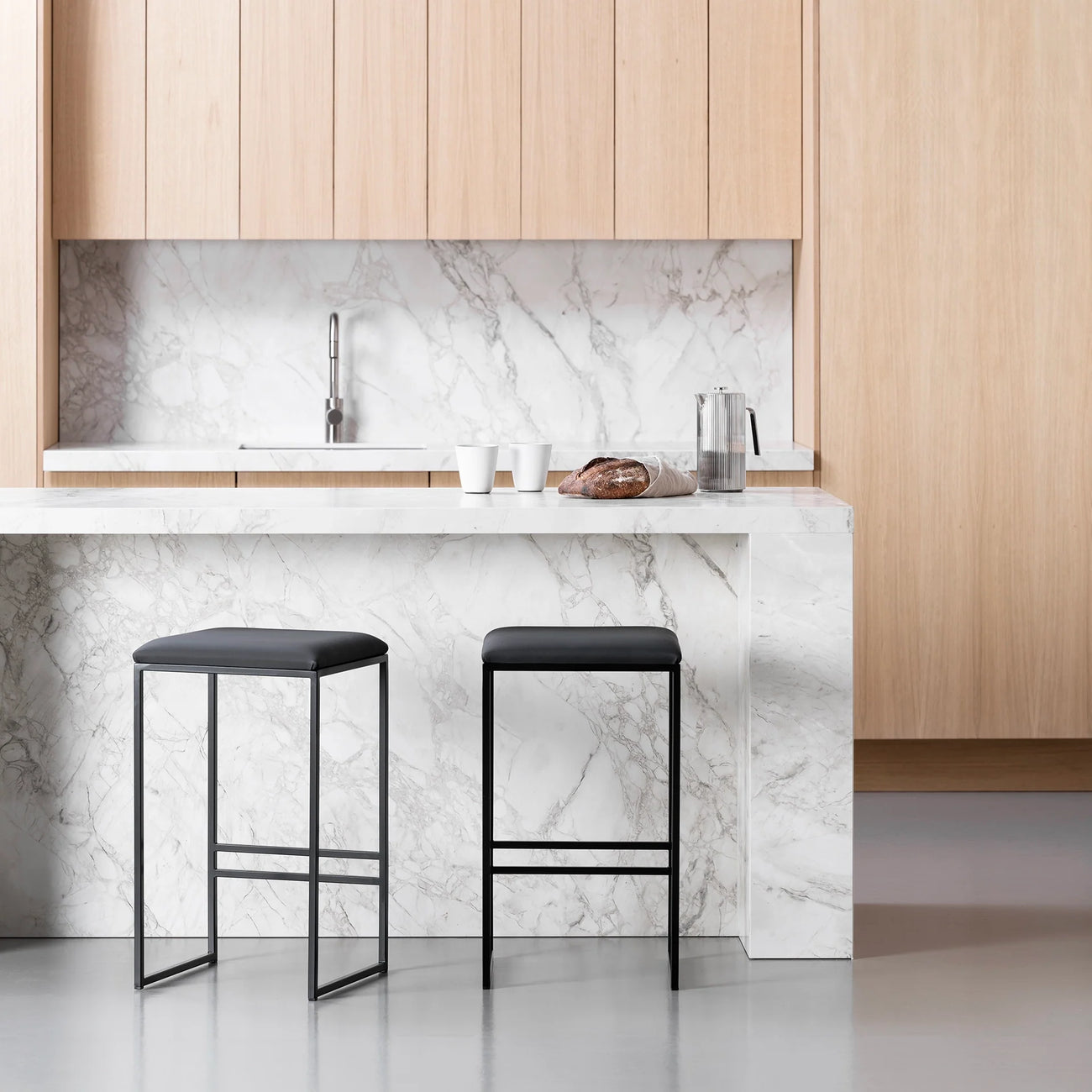 Svea bar stools in black leather at a modern kitchen island with marble countertop.