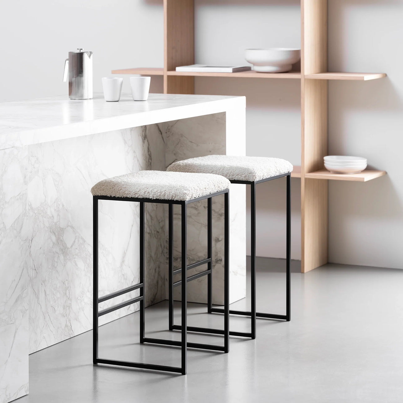 Svea bar stools in black frame with ivory bouclé seat, modern high stools at a marble kitchen counter.