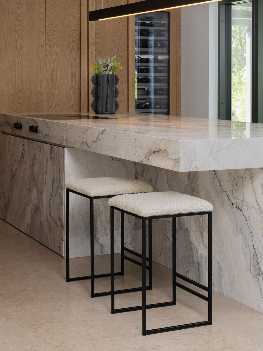 Bar Stool Svea in black with ivory bouclé fabric beside a modern marble kitchen island.