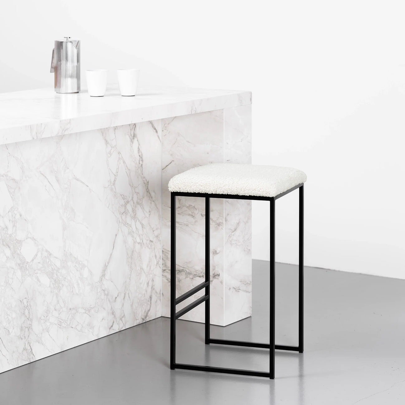 Svea bar stool with black frame and ivory bouclé seat, featuring a modern design in a contemporary kitchen setting.