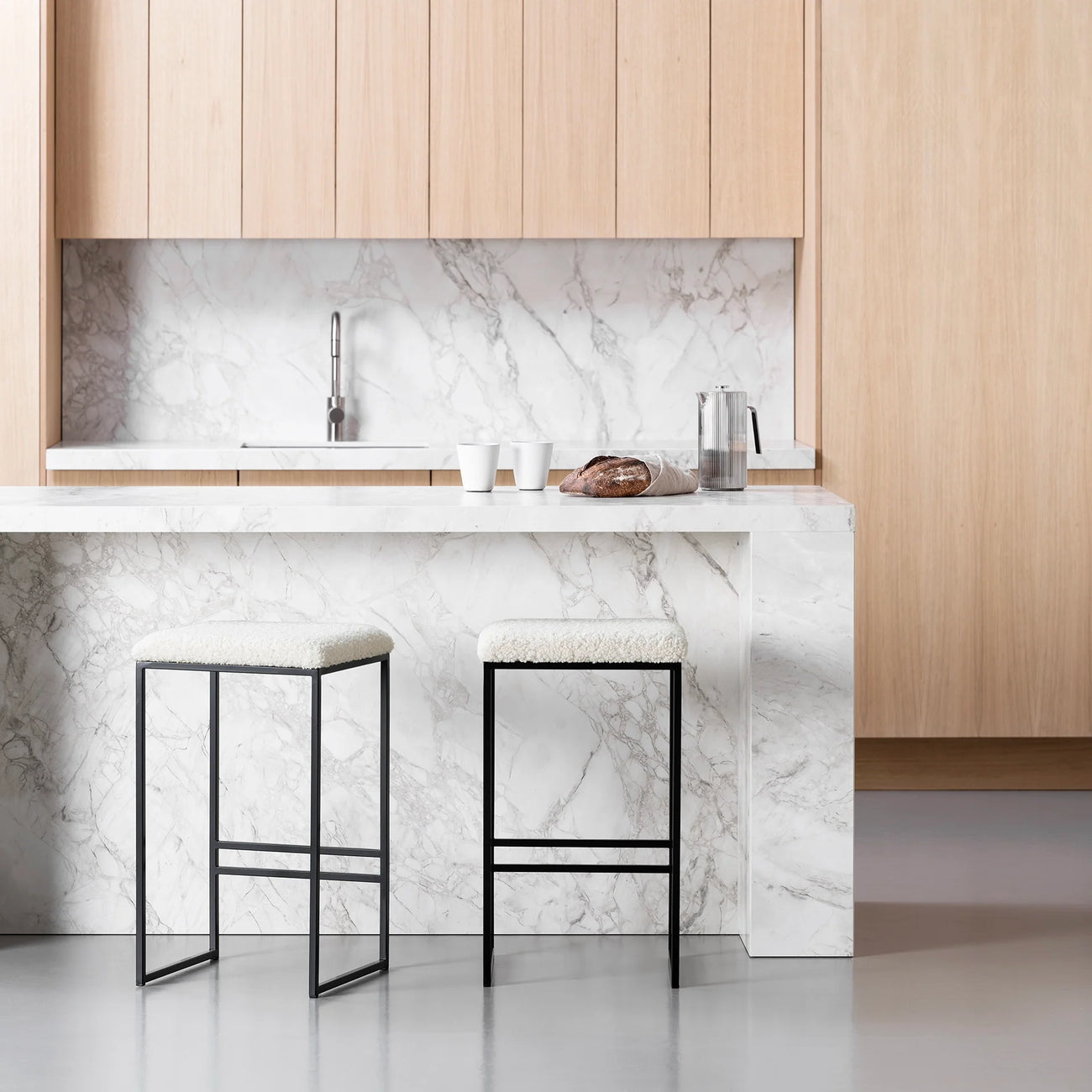 Svea bar stools in black frame with ivory bouclé seats, set against a modern marble kitchen countertop.