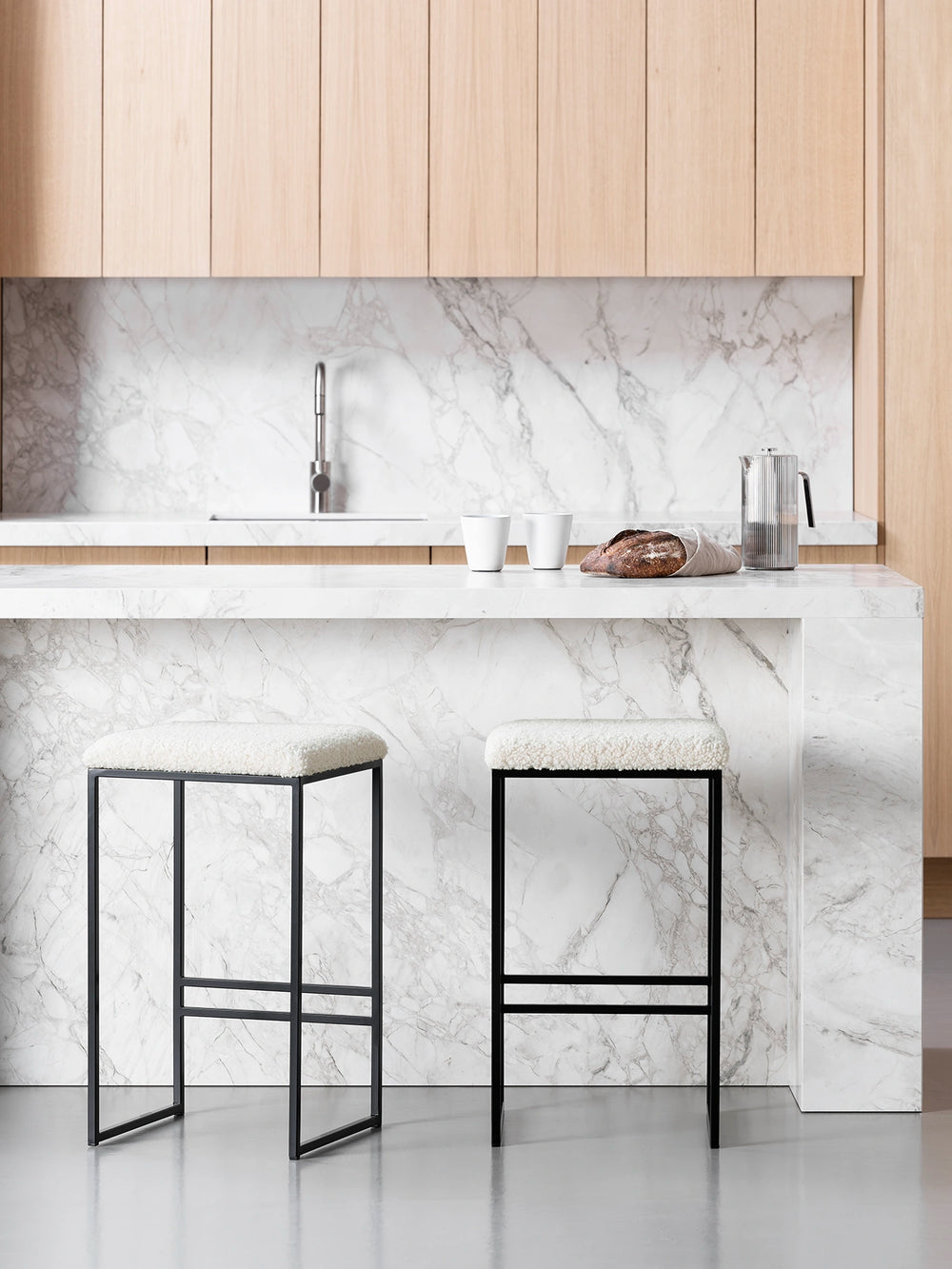 Bar Stool Svea in black and ivory bouclé placed at a modern kitchen island with marble countertop.
