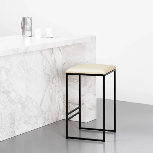 Svea black bar stool with sand leather seat against a marble countertop, showcasing a modern and minimalistic design.
