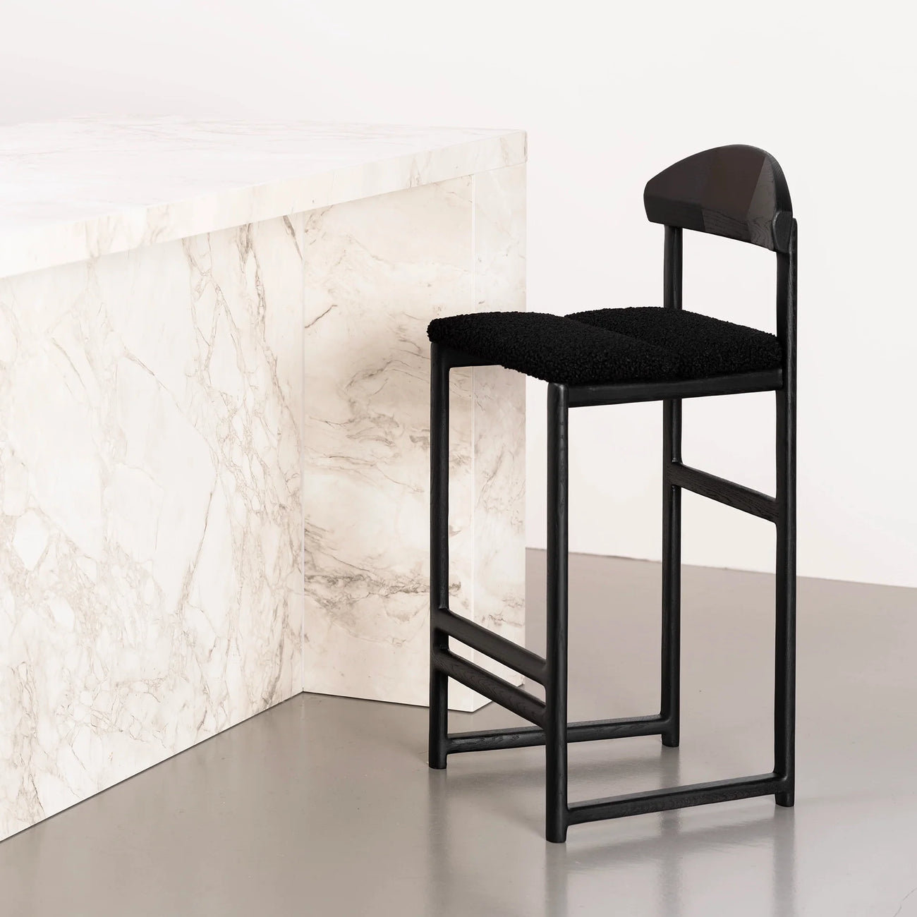 Ted Bar stool in black oak with a black bouclé seat, styled against a marble counter for a sleek, modern aesthetic.