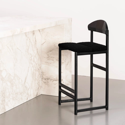 Ted Bar stool in black oak with a black bouclé seat, styled against a marble counter for a sleek, modern aesthetic.