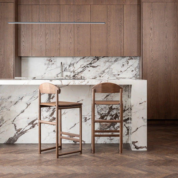 Ted bar stools in dark oak with wooden backrests against a sleek marble kitchen island, showcasing modern Nordic design.