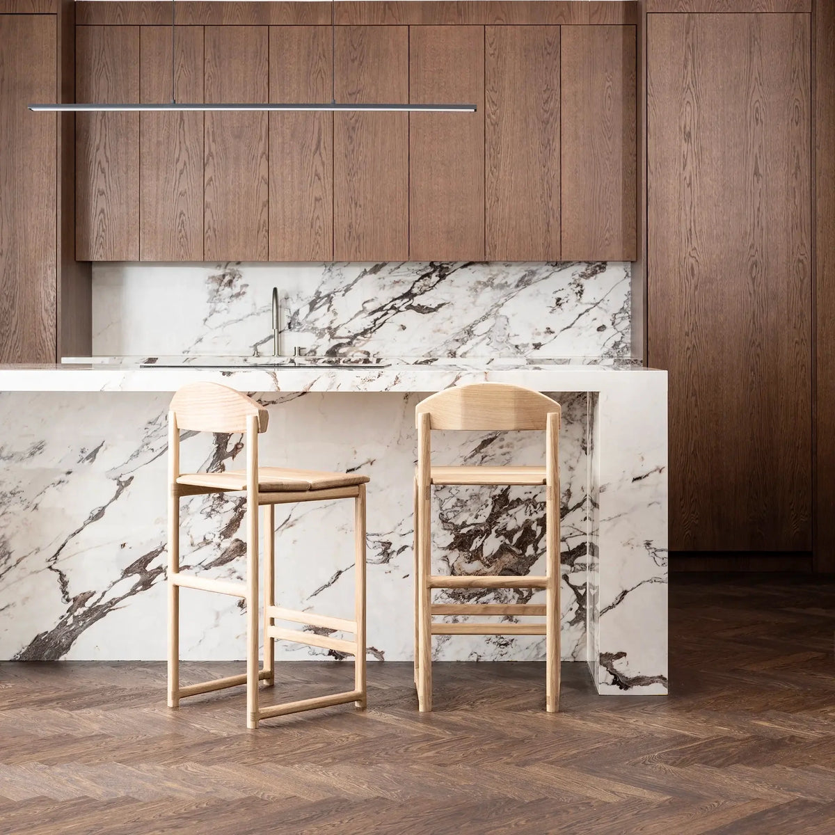 Minimalistic solid oak Ted bar stools in a modern kitchen with marble countertop and wooden cabinets.