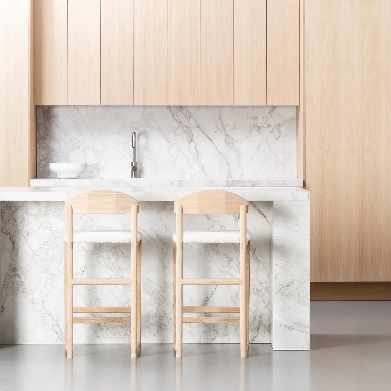 Oak bar stools with ivory bouclé seats in a modern kitchen design featuring a marble countertop.