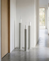 Thomas candleholders in beige with glass cylinders, placed in a minimalist Scandinavian hallway with concrete flooring, white walls, and natural light from wooden-framed windows.