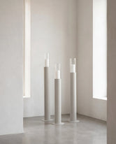 Thomas candleholders in beige with glass cylinders, placed in a minimalist interior with soft white walls and polished concrete flooring, creating a calm Scandinavian atmosphere.