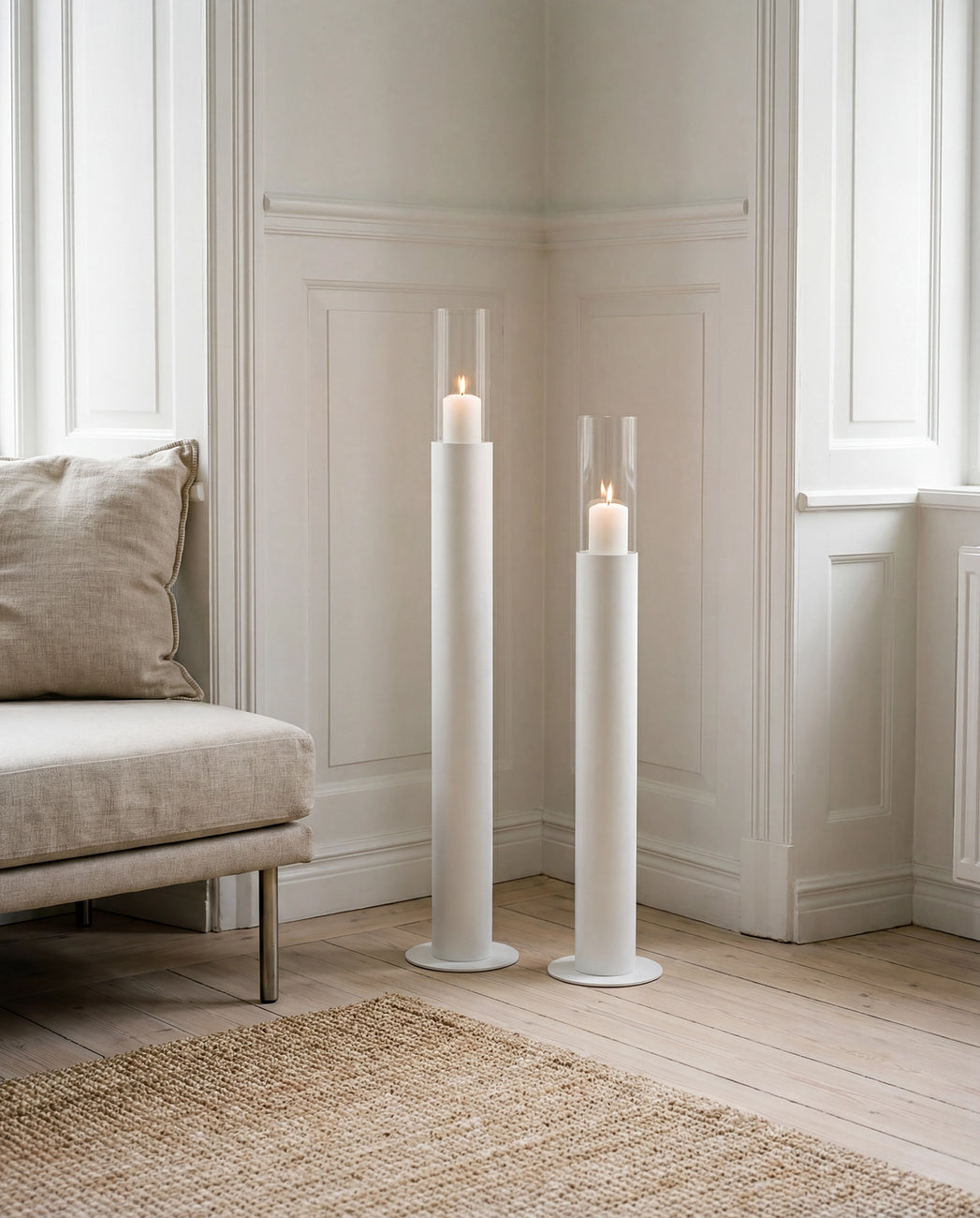 Thomas candleholders in white with glass cylinders and lit candles, styled in a classic Scandinavian interior with wall paneling, light wooden flooring, and a neutral lounge chair.