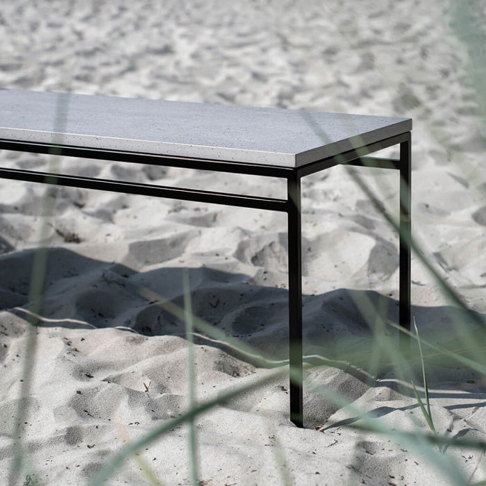 Wilma outdoor bench in black with sleek Keon dekton top, set against sandy background, perfect for gardens.
