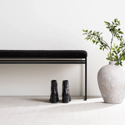 Wilma black bouclé bench with clean lines, minimalist design, and stylish black boots beside a textured vase.